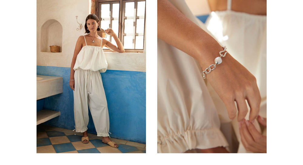Editorial spread of woman wearing a white bubble tank paired with white pants. On the opposite side is a closeup of a silver chain bracelet with pearl and hook detailing.